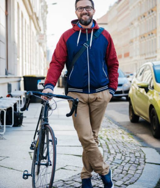 A portrait of a man standing beside his bicycle smiling on a city street.